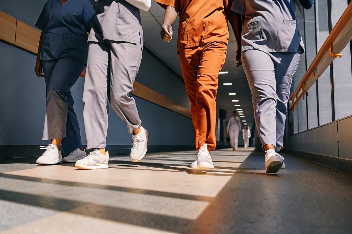 Nurses in scrubs and sneakers walking together down a hospital hallway mid-shift