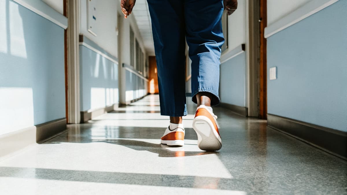 Close low-angle shot of a nurse in navy scrubs and orange and white sneakers walking down a hospital corridor