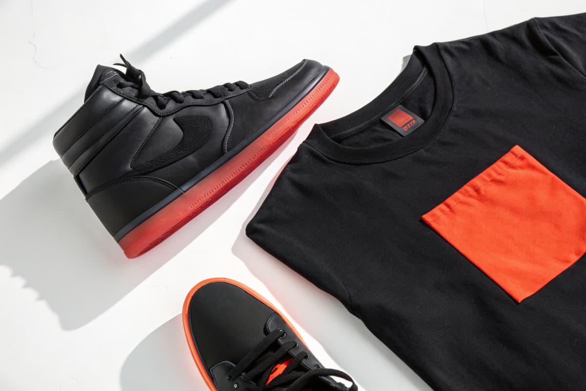 Black high-top sneaker with a translucent fire red sole laid flat next to a folded black tee with a matching fire red chest block