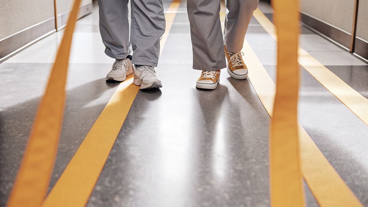 Close crop of two healthcare workers walking down a hospital hallway, navy scrubs, orange badge reel lanyards swinging, white sneakers with bright orange sole accents in motion on a polished floor